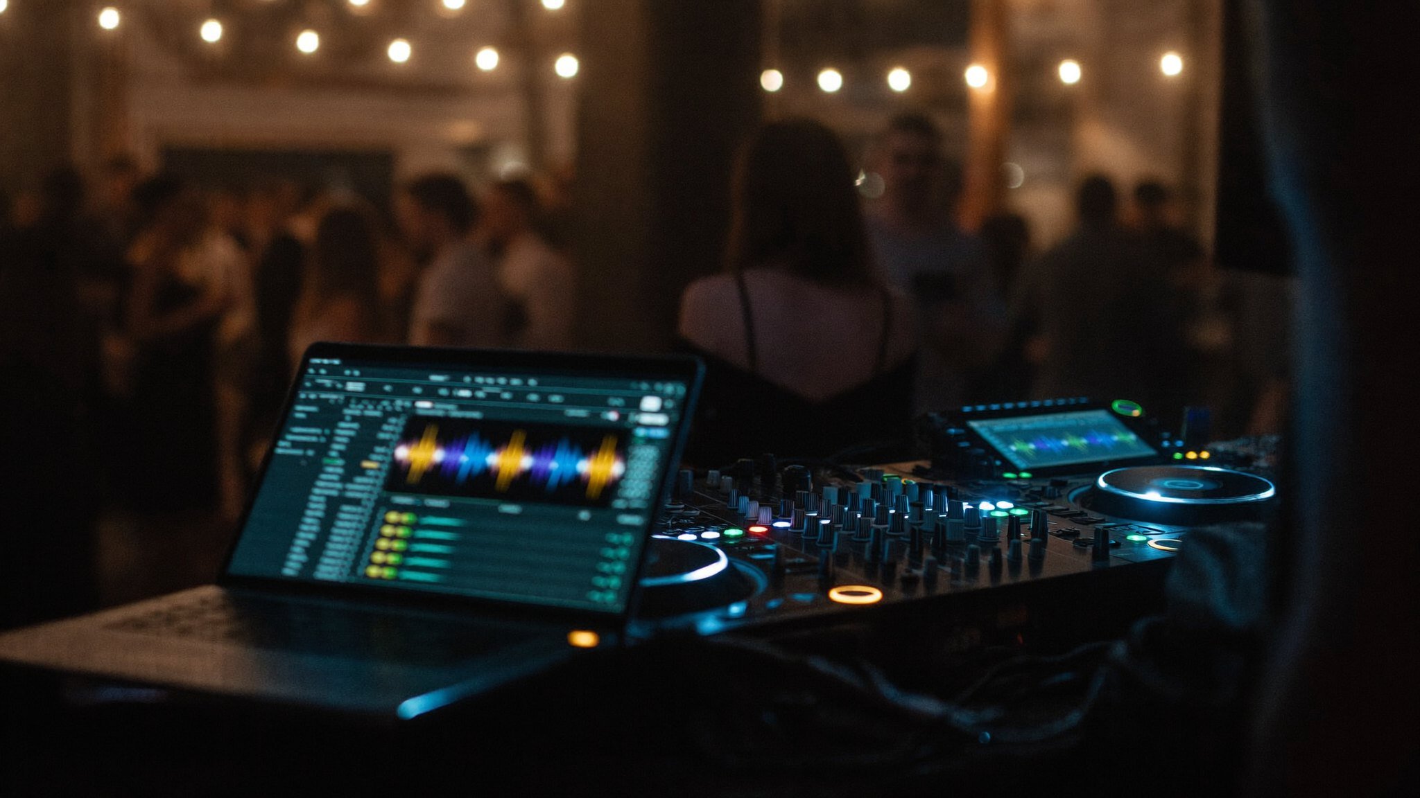 DJ controller and laptop glowing mid-set at a dark loft event