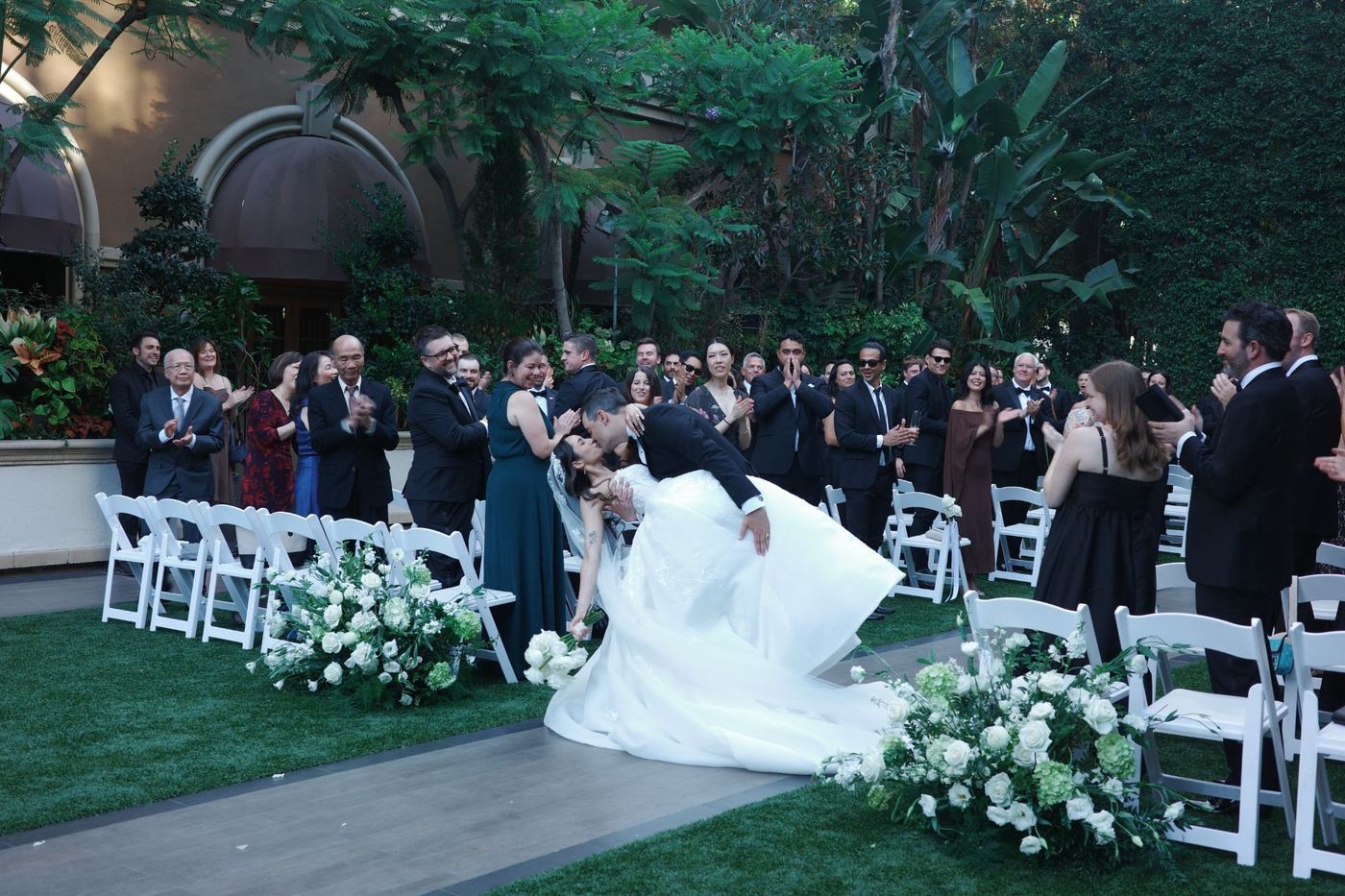 Chris and Eileen kissing at the end of their outdoor garden ceremony at the Four Seasons Hotel Los Angeles at Beverly Hills, guests applauding on both sides of the aisle