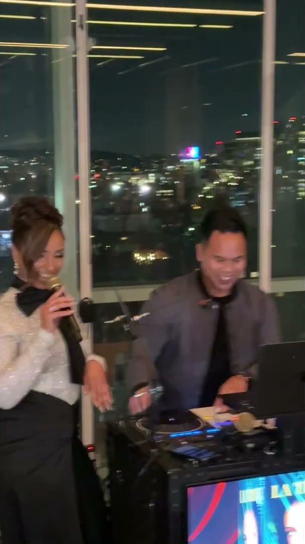 Mýa on the microphone beside DJ MOJOE's booth at the W Hollywood, LA skyline behind them